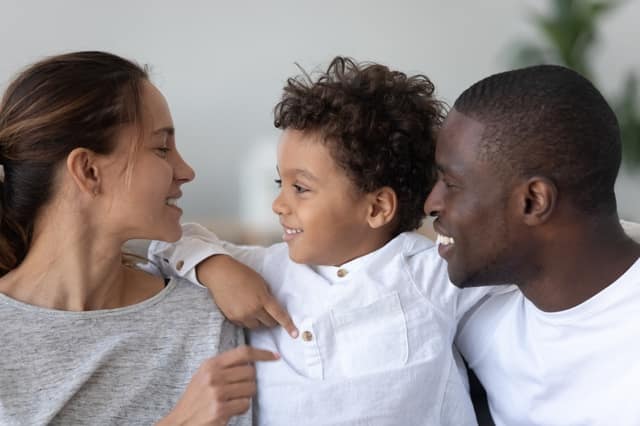 -giovani-genitori-multietnici-sorridenti-abbracciano-le-coccole-con-il-piccolo-figlio-birazziale-carino-a-casa