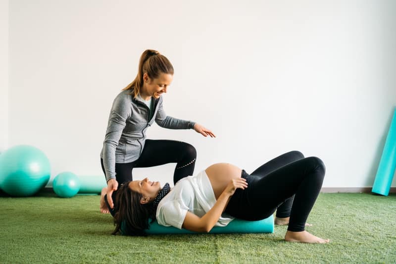 Donna incinta che fa esercizio di pilates e palla fitness con allenatore. Felice futura madre che si prepara al parto.