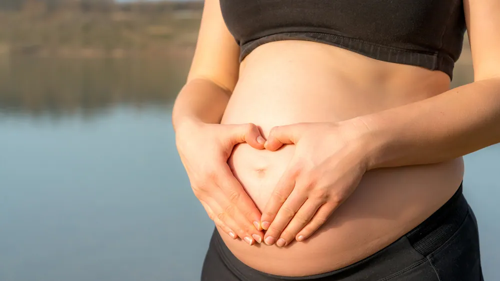 Donna che tiene la sua pancia con le mani e forma un cuore
